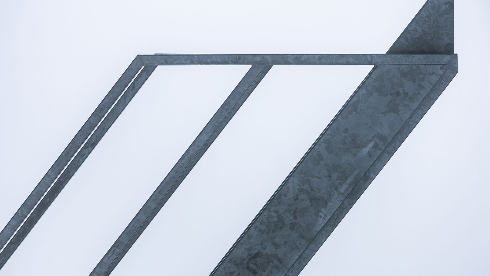 Diagonal steel beams meeting at clean angles against a pale sky.